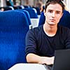 Handsome young man using his laptop computer while on the train (shallow DOF; color toned image)