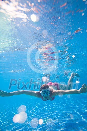 Underwater swimming: young woman swimming underwater in a pool, wearing a diving mask Underwater swimming: young woman swimming underwater in a pool, wearing a diving mask