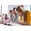 young pretty female college student sitting in a classroom full of students during class