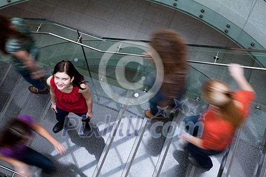 At the university/college - Students rushing up and down a busy stairway - confident pretty young female student looking upwards (color toned image) At the university/college - Students rushing up and down a busy stairway - confident pretty young female student looking upwards (color toned image)