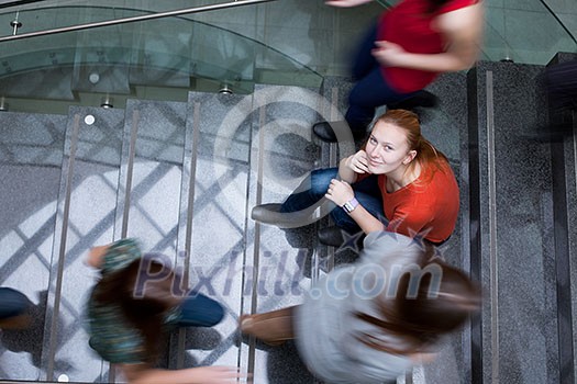 At the university/college - Students rushing up and down a busy stairway - confident pretty young female student looking upwards (color toned image) At the university/college - Students rushing up and down a busy stairway - confident pretty young female student looking upwards (color toned image)