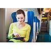 Young woman using her tablet computer while traveling by train