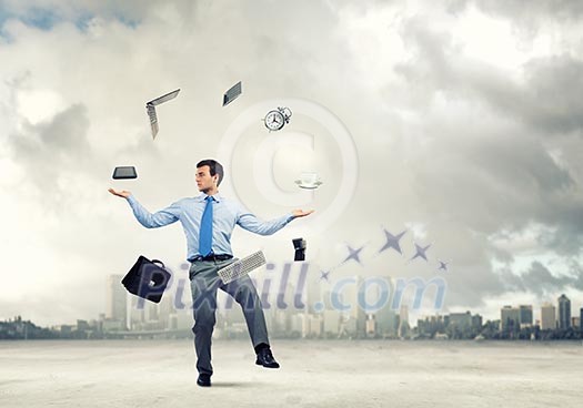 Young businessman juggling with business items against urban scene Young businessman juggling with business items against urban scene