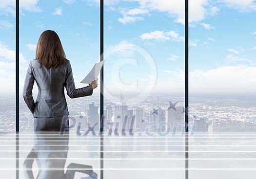 Businesswoman standing with back against office window holding documents in hand