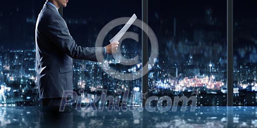 Businessman standing against office window reading documents Businessman standing against office window reading documents