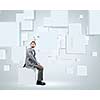 Young handsome businessman sitting on white cube