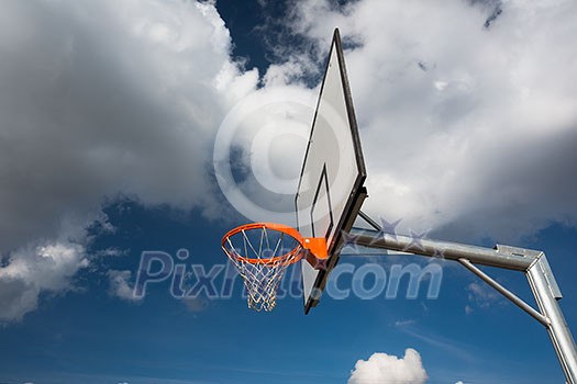 Basketball hoop against lovely blue summer sky with some fluffy white clouds Basketball hoop against lovely blue summer sky with some fluffy white clouds