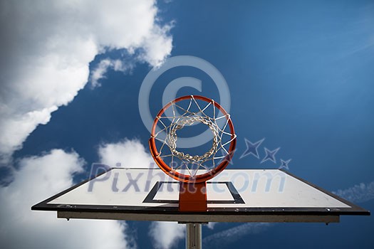 Basketball hoop against lovely blue summer sky with some fluffy white clouds Basketball hoop against lovely blue summer sky with some fluffy white clouds