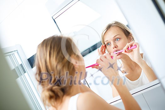 Pretty female brushing her teeth in front of mirror in the morning, making silly faces, checking her skin Pretty female brushing her teeth in front of mirror in the morning, making silly faces, checking her skin