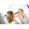 Pretty female brushing her teeth in front of mirror in the morning, making silly faces, checking her skin