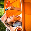 Pretty, young woman camping outdoors, lying in the tent in the morning, using her smart phone