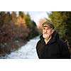 Portrait of a senior man, outdoor on a snowy forest path. Enjoying the crisp fresh air, watching the Sun go down.