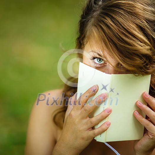 Cute young woman covering her face with a book she is reading Cute young woman covering her face with a book she is reading