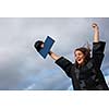 Pretty, young woman celebrating joyfully her graduation - spreading wide her arms, holding her diploma, savouring her success (color toned image; shallow DOF)