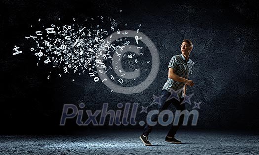 Funny image of young man trying to escape from flying letters Funny image of young man trying to escape from flying letters