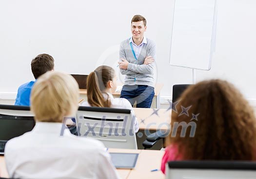 Young teacher in classroom standing in front of class Young teacher in classroom standing in front of class