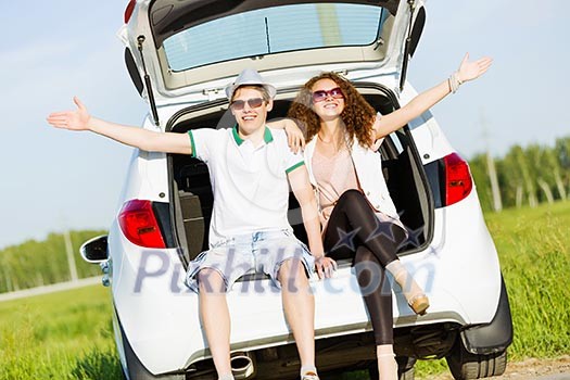 Young happy couple sitting in car trunk outdoor Young happy couple sitting in car trunk outdoor