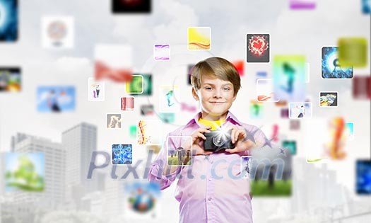 Image of cute boy holding photo camera standing among photos Image of cute boy holding photo camera standing among photos