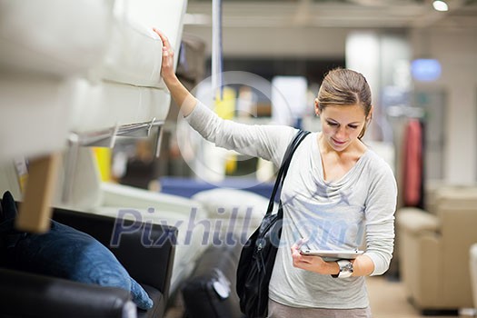 Young woman shopping for furniture in a furniture store, using her tablet computer to compare prices/check for dimensions Young woman shopping for furniture in a furniture store, using her tablet computer to compare prices/check for dimensions