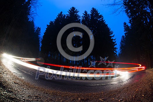 Cars going fast through a curve on a forest road at dusk, on a rainy day - i.e. Potentially dangerous driving conditions