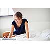 Elegant, smart, young woman using her tablet computer in bed (shallow DOF; color toned image)