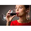 Elegant young woman in a red dress, having a glass of red wine