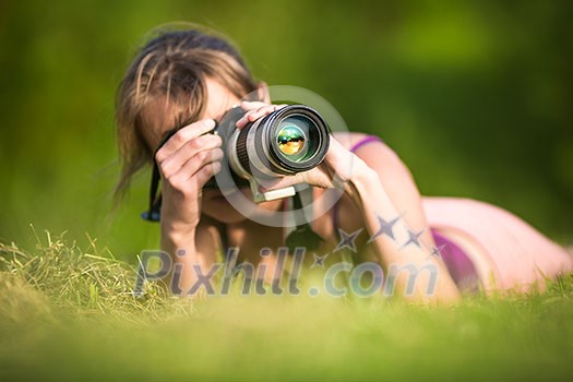 Pretty female photographer lying in grass, on a lovely summer day, taking pictures with her DSLR camera and a telephoto lens Pretty female photographer lying in grass, on a lovely summer day, taking pictures with her DSLR camera and a telephoto lens