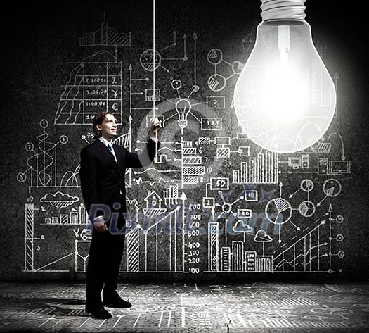 Businessman switching on light bulb with business sketches at background Businessman switching on light bulb with business sketches at background