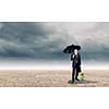 Young businessman with umbrella protecting sprout growing in desert