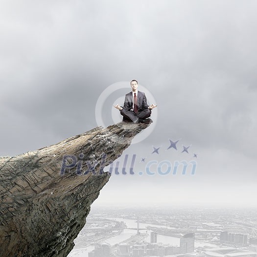 Young businessman sitting lotus pose on edge of rock mountain Young businessman sitting lotus pose on edge of rock mountain