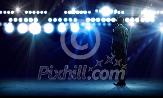 Rear view of businessman standing in lights of stage Rear view of businessman standing in lights of stage