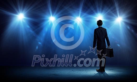 Rear view of businessman standing in lights of stage Rear view of businessman standing in lights of stage