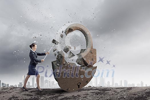 Young angry businesswoman crashing stone lock with hammer Young angry businesswoman crashing stone lock with hammer