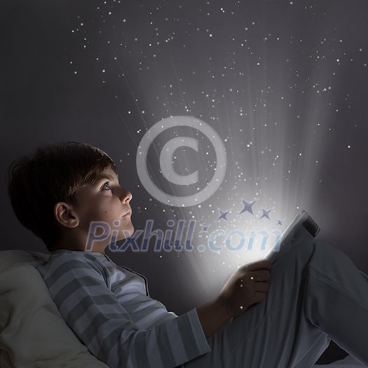 Cute boy sitting in bed and using tablet pc Cute boy sitting in bed and using tablet pc