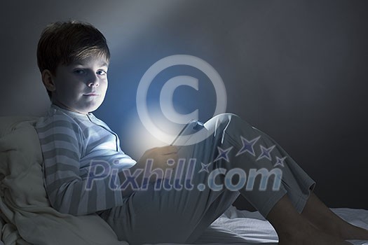 Cute boy sitting in bed and using tablet pc Cute boy sitting in bed and using tablet pc