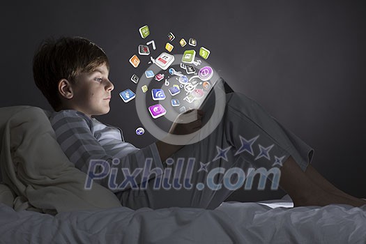 Cute little boy sitting in bed and using tablet pc Cute little boy sitting in bed and using tablet pc