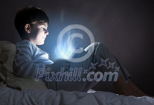 Cute boy sitting in bed and using tablet pc Cute boy sitting in bed and using tablet pc