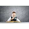 Schoolgirl examining opened book with magnifying glass
