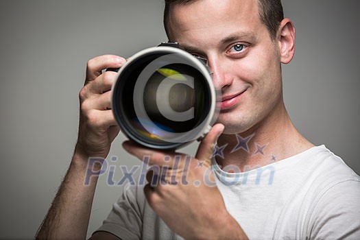 Young pro photographer with digital camera - DSLR and a huge telephoto lens in his well equiped studio, taking photos (color toned image; shallow DOF) Young pro photographer with digital camera - DSLR and a huge telephoto lens in his well equiped studio, taking photos (color toned image; shallow DOF)