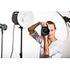Pretty, female pro photographer with digital camera - DSLR and a huge telephoto lens in her well equiped studio, taking photos (color toned image; shallow DOF)