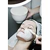 Young beautiful woman receiving cosmetic facial mask in spa beauty salon and relax