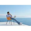handsome young man relaxing and working on laptop computer at home balcony while looking sunset