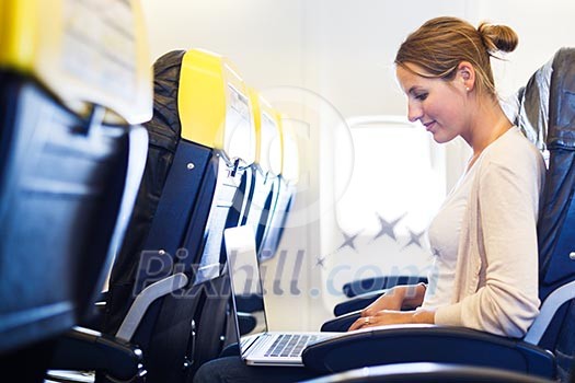 Young woman working on her laptop computer on board of an airplane during the flight Young woman working on her laptop computer on board of an airplane during the flight