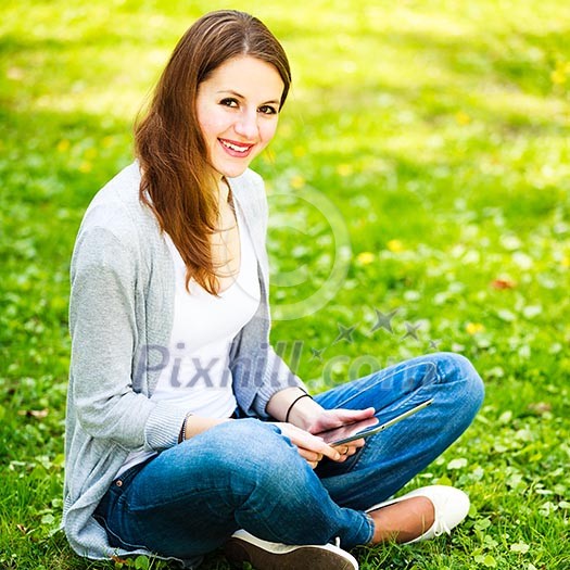 Young woman using her tablet computer while relaxing outdoors in a park on a lovely spring day Young woman using her tablet computer while relaxing outdoors in a park on a lovely spring day