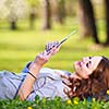 Young woman using her tablet computer while relaxing outdoors in a park on a lovely spring day