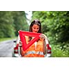 Young female driver wearing a high visibility vest, calling the roadside service/assistance after her car has broken down