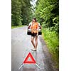 Young female driver wearing a high visibility vest, calling the roadside service/assistance after her car has broken down