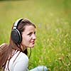 portrait of a pretty young woman listening to music on her mp3 player outdoors (daydreaming)
