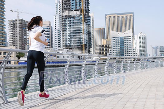 Running in city park. Woman runner outside jogging at morning with Dubai urban scene in background Running in city park. Woman runner outside jogging at morning with Dubai urban scene in background