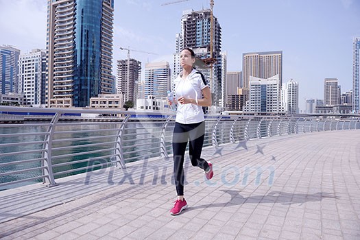 Running in city park. Woman runner outside jogging at morning with Dubai urban scene in background Running in city park. Woman runner outside jogging at morning with Dubai urban scene in background